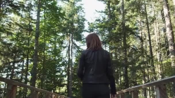 年轻的女人走在木头路上，在森林里有栏杆 — 图库视频影像
