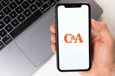 C ve A, internetten kıyafet, ayakkabı ve aksesuar almak için uygun bir mobil uygulama. Adam elinde açık bir başvuru formu olan bir akıllı telefon tutuyor. İnternetten alışveriş Kasım 2021, San