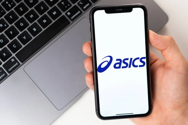 Asics é uma aplicação móvel conveniente para comprar roupas, sapatos e acessórios online. Man está segurando um smartphone com um aplicativo aberto em sua mão. Compras online novembro 2021, San — Fotografia de Stock