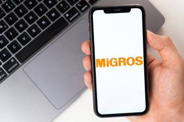Akıllı telefon ekranında MiGROS mobil uygulaması. Açık bir dizüstü bilgisayarın yanında bir adamın elinde cep telefonu. Kasım 2021, San Francisco, ABD