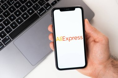 AliExpress mobil uygulaması akıllı telefon ekranında. Açık bir dizüstü bilgisayarın yanında bir adamın elinde cep telefonu. Kasım 2021, San Francisco, ABD