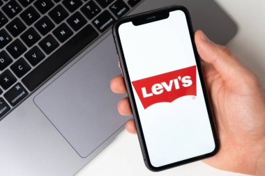 Levis uygulaması, arka planda dizüstü bilgisayarı olan bir adamın elinde akıllı telefon ekranında. Cep telefonuyla online alışveriş Kasım 2021, San Francisco, ABD
