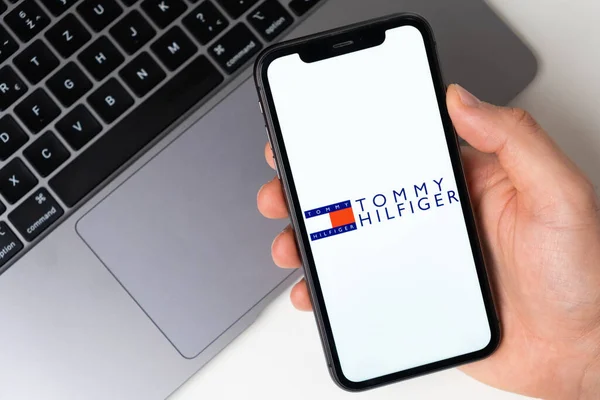 Logotipo de aplicação Tommy Hilfiger para compras online na tela do telefone móvel. Mão de homem segurando um smartphone com aplicação novembro 2021, San Francisco, EUA — Fotografia de Stock