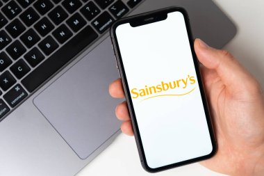 Sainsbury uygulaması akıllı telefonda açık. Adam elinde bir cep telefonu tutuyor, şirket başvurusu ekranda açık. Güvenli online alışveriş. Kasım 2021, San Francisco