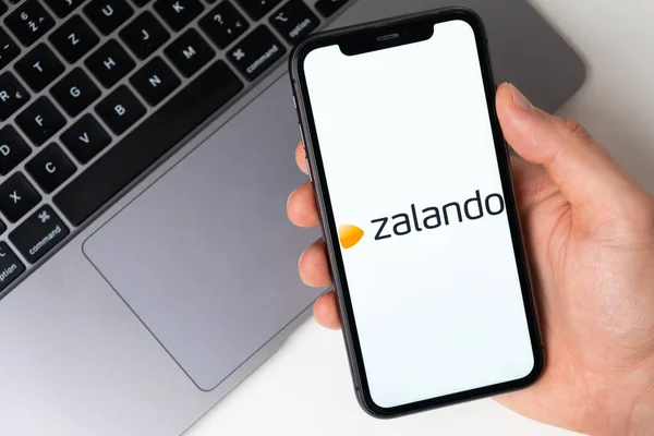Zalando应用在智能手机屏幕上，手持笔记本电脑作为背景。2021年11月在美国旧金山通过手机进行网上购物 — 图库照片