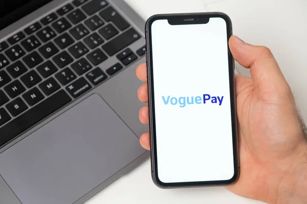 VoguePay finanční platforma pro převod peněz pomocí smartphonu. Muž drží mobilní telefon s aplikací na obrazovce a notebook na pozadí. Listopad 2021, San Francisco, USA — Stock fotografie
