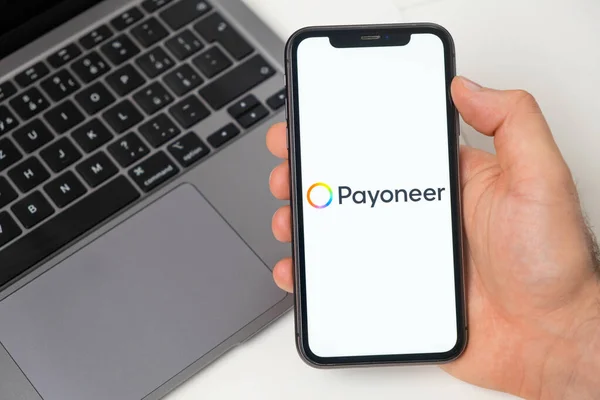 Payoneer finanční platforma pro převod peněz pomocí smartphonu. Muž drží mobilní telefon s aplikací na obrazovce a notebook na pozadí. Listopad 2021, San Francisco, USA — Stock fotografie