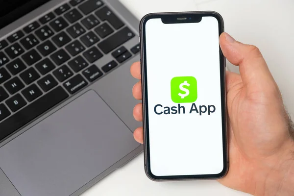 Cash App pénzügyi platform a pénzátutalás segítségével okostelefon. Férfi kéz tartja mobiltelefon alkalmazás a képernyőn, és notebook a háttérben. 2021. november, San Francisco, USA — Stock Fotó