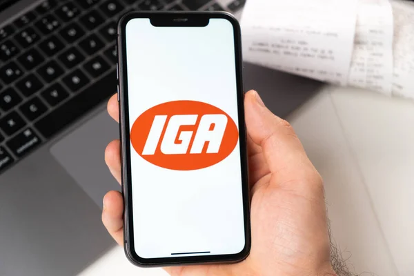Aplicação IGA na tela do iPhone da Apple na mão homem e laptop em segundo plano. Conceito de compras on-line novembro 2021, San Francisco, EUA — Fotografia de Stock