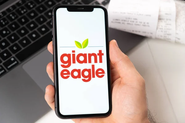 Aplicação de águia gigante na tela do iPhone da Apple em mão de homem e laptop em segundo plano. Conceito de compras on-line novembro 2021, San Francisco, EUA — Fotografia de Stock