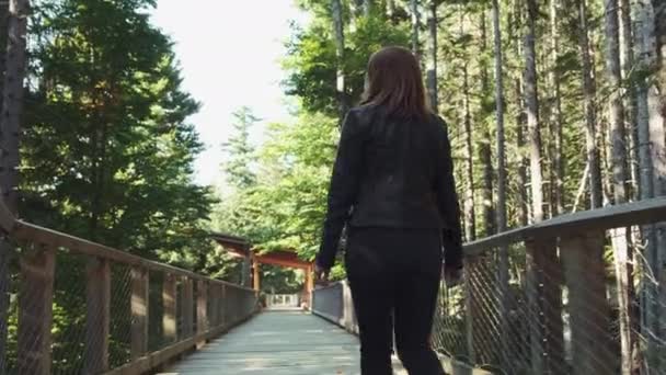 Brunette woman strolls on wooden road footbridge in forest — 图库视频影像