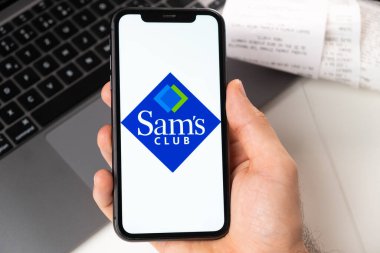 Apple iPhone ekranındaki Sams Club uygulaması arka planda erkek eli ve dizüstü bilgisayarda. Çevrimiçi alışveriş kavramı Kasım 2021, San Francisco, ABD