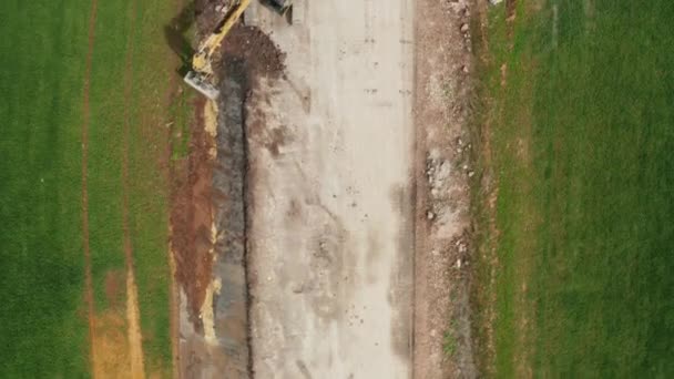 Aerial view of excavator collects soil from the green field — стоковое видео