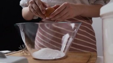 Lady breaks egg into bowl with sugar for making dessert