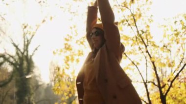 Cheerful lady in coat and warm hat dances in autumn forest