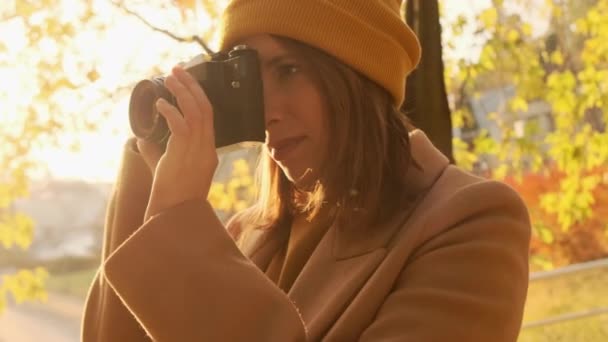 Жінка в пальто з камерою фотографується в осінньому лісі — стокове відео