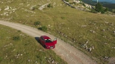 Aerial view of Skoda Scala red car in the field with spinning wind turbines highly in the mountains on the background, October 2021, Vratarusa, Croatia.