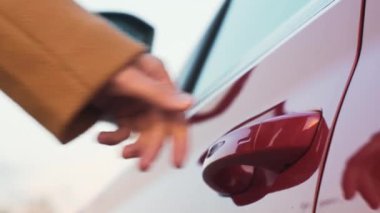 A womans hand brings a finger to the car door handle, closes it and the side mirror folding 