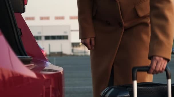 A business woman lowers the handle on a suitcase and puts it in the trunk of a red car — Stok video
