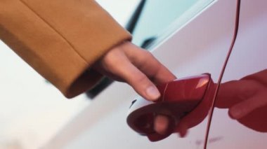A woman brings her hand to the red car door handle and opens it, side mirror unfolding. Rent car concept 