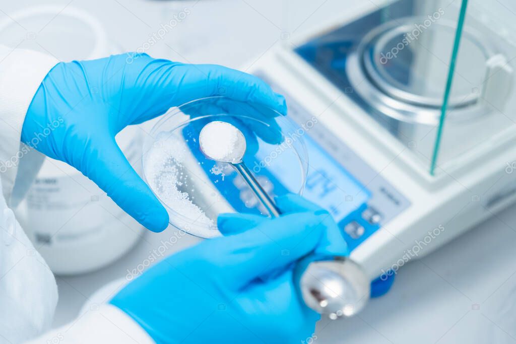 Digital analytical balance for accurate weighing of samples. Close up scientist hands in rubber gloves use metal spatula for weighing white powder of the substance