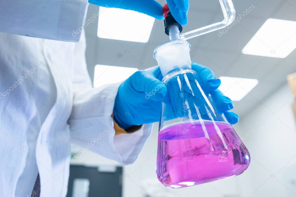 Close up scientist uses a titration method of analysis to study chemical properties of the water sample. Scientist holding Erlenmeyer flask with pink solution. 