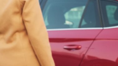 Woman in coat gets into red car to ride along city street