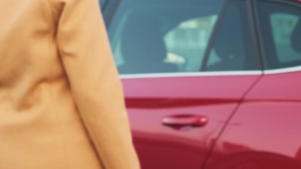 Woman in coat gets into red car to ride along city street — Stockvideo