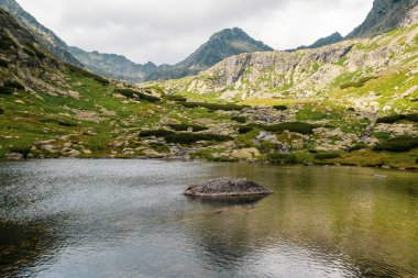 Beautiful lake in High Tatra mountains with stones in the middle and clouds reflections on water. 