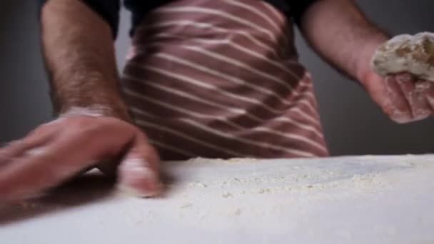 男パン屋は小麦粉を配布し、テーブルの上に生の生地を置く — ストック動画