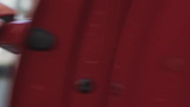 Kadın elini arabanın kırmızı sapına koyar, kapıyı açar ve kahverengi bir ceketin içinde oturur.