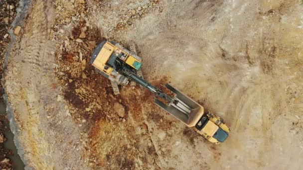 Gelber Bagger von oben hebt Mineralien aus der offenen Grube auf und verlädt sie auf den LKW — Stockvideo