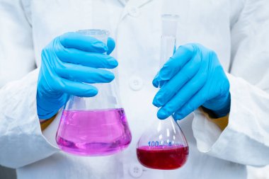 Bilim adamı kimya laboratuvarındaki mataralarda parlak çözümlerle deneyler yapıyor. Modern mikrobiyoloji merkezinde çalışan bir araştırmacı.