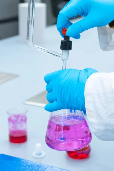 Ο εργαζόμενος σε κλειστό εργαστήριο χρησιμοποιεί μέθοδο τιτλοδότησης για τη μελέτη των χημικών ιδιοτήτων του δείγματος νερού. Επιστήμονας που κρατά τη φιάλη Erlenmeyer με ροζ διάλυμα. — Φωτογραφία Αρχείου