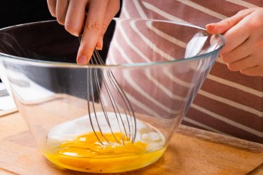 Mutfaktaki ahşap masada hamur yapmak için yumurta çırpan bir kadının ellerine yaklaş. Ev yapımı yemek. 