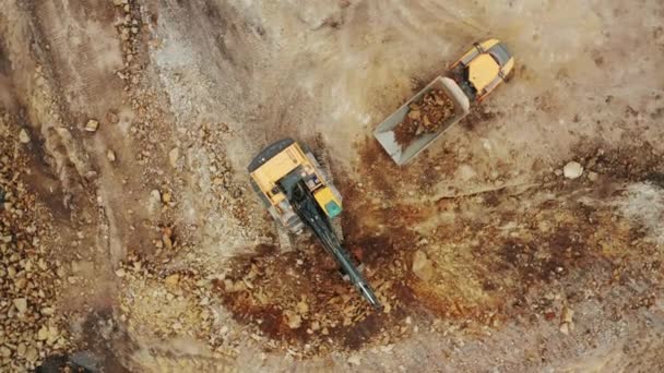 Gelber Bagger von oben hebt Mineralien aus der offenen Grube auf und verlädt sie auf den LKW — Stockvideo