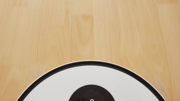 Un robot aspirateur blanc court sur le sol en bois. Nettoyage facile de la maison. — Video