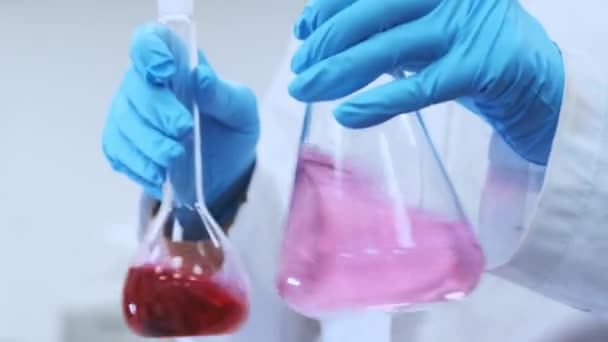 Cientista de pesquisa médica prepara soluções em laboratório de ciência aplicada. Mãos de cientista próximas em luvas de borracha misturando amostras rosa para análise química — Vídeo de Stock