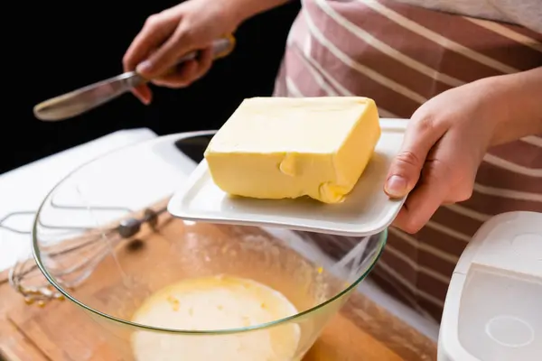 生地の準備プロセス.女性の手は黒の背景にケーキを焼くための混合ボウルにバターを追加します。ペストリーの自家製レシピ — ストック写真