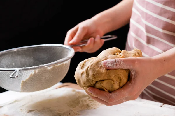 女性を閉じます黒の背景にケーキやパン屋のための生地の準備のための混合ボウルにふるいを通して小麦粉をふるいます.自家製ペストリーのための生地をこねる — ストック写真