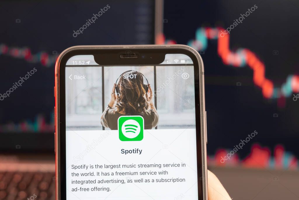 Spotify stock price decrease on the trading market with downtrend line graph bar chart on the background. Man holding a mobile phone with company logo, February 2022, San Francisco, USA.