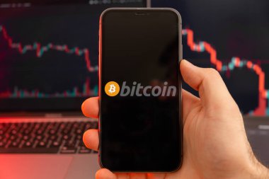 Şifreli para piyasası analizinin Bitcoin BTC uygulaması insan eliyle cep telefonu ekranında ve iniş trendleri grafiklerinde arka planda, Şubat 2022, San Francisco, ABD