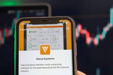Veeva Systems borsada yükselen hisse senedi fiyatları ve arka planda yükselen grafikler. Şirket logosu olan bir cep telefonu taşıyan adam, Şubat 2022, San Francisco, ABD. 