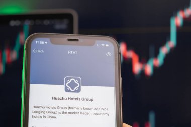 Huazhu Hotels Group hisse senedi fiyatları yükseldi ve arkaplanda grafikler var. Ekranda logosu olan akıllı telefonu tutan adam elleri, Şubat 2022, San Francisco, ABD