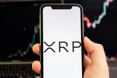Akıllı telefon ekranındaki XRP kripto para birimi logosu yeşil arka plandaki grafikte büyüyen bir eğilimle birlikte 