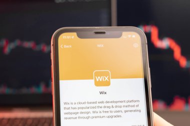 Piyasada Wix hisse senedi fiyatları düşerken, arka planda grafikler çizelgesi var. Şirket logosu olan bir cep telefonu taşıyan adam, Şubat 2022, San Francisco, ABD