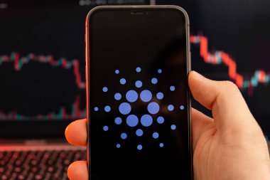 Cardano ADA insan eliyle cep telefonu ekranındaki kripto para piyasası analizi uygulaması ve arka plandaki eğilim grafikleri ticaret verileri, Şubat 2022, San Francisco, ABD