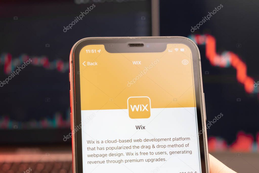 Wix stock price decrease on the trading market with downtrend line graph bar chart on the background. Man holding a mobile phone with company logo, February 2022, San Francisco, USA.