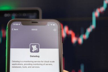 Datadog hisse senedi fiyatları yükseldi ve arka planda grafikler var. Ekranda logosu olan akıllı telefonu tutan adam elleri, Şubat 2022, San Francisco, ABD