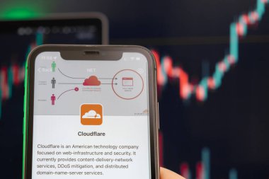 Cloudflare hisse senedi fiyatlarında artış ve arka planda grafikler. Ekranda logosu olan akıllı telefonu tutan adam elleri, Şubat 2022, San Francisco, ABD